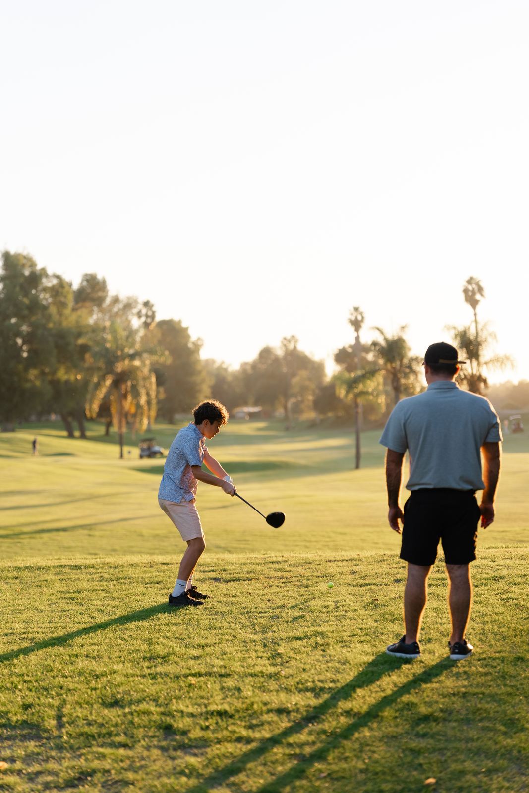 Kid swinging on the tee as his dad looks on