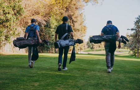 three golfers carrying sets of golf clubs