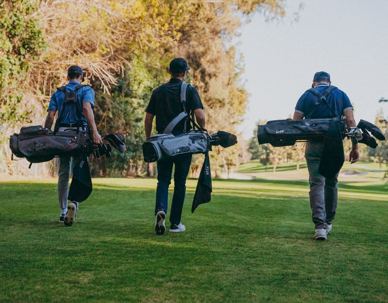 three golfers carrying sets of golf clubs