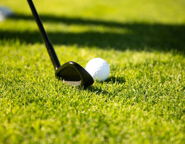 A golf wedge lined up behind a golf ball on turf