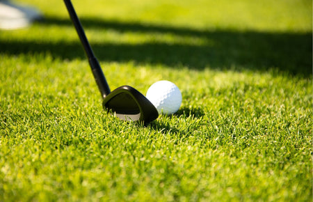 A golf wedge lined up behind a golf ball on turf