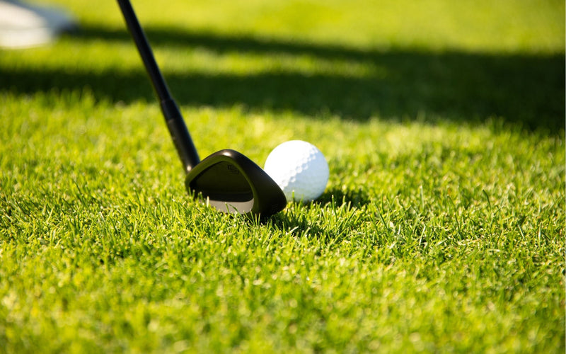 A golf wedge lined up behind a golf ball on turf