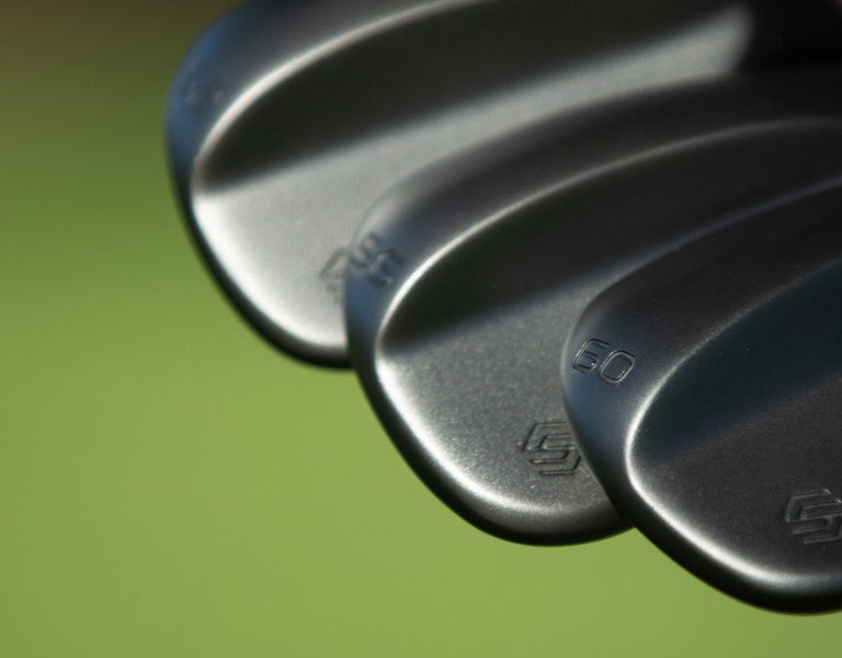 Three Stix Perform wedges fanned in stealth black against a soft green course backdrop.