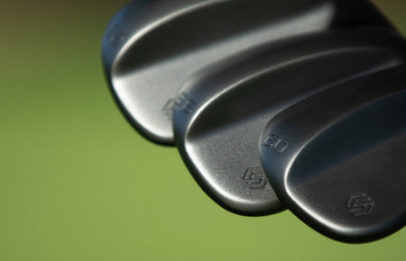 A golfer's wedge mid-swing in late-afternoon light, ball on a tight lie.