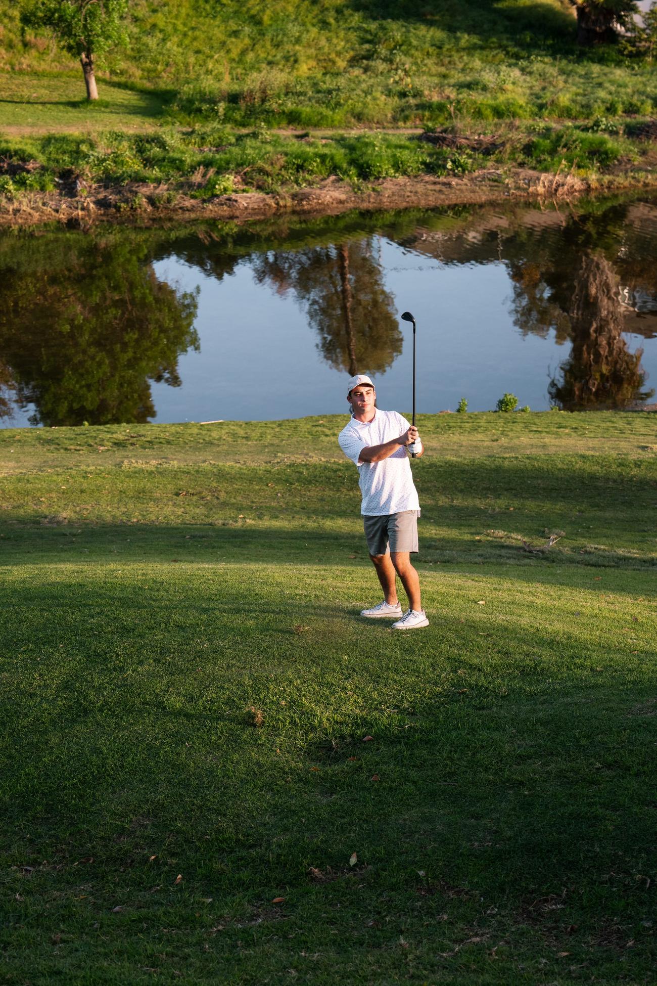 A golfer holds his finish after an approach shot over the water